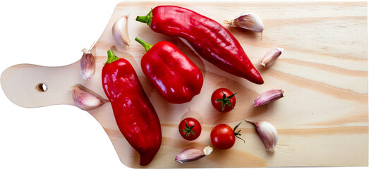 Wooden cutting board with red peppers, cherry tomatoes and garlic cloves.