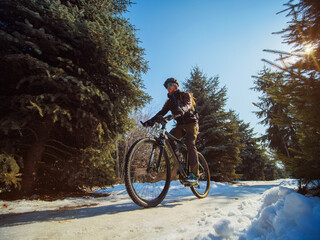 A bearded guy rides a bike in the winter in the park. Active pastime in winter. Bicycle as an ecological transport