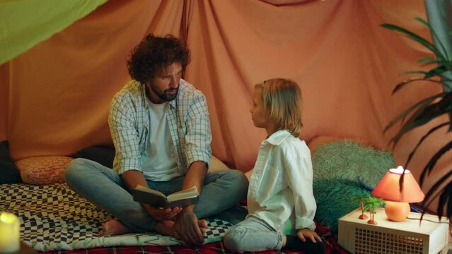 A Blonde Little Boy And A Handsome Father With Brown Hair And Talking To Eachother And Discussing A Book Inside Their Amazing Blanket Fort