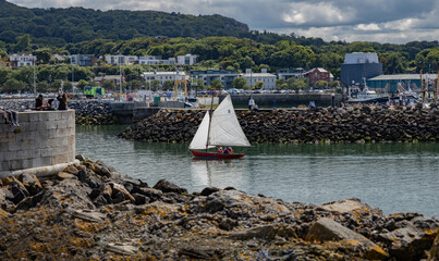 Żaglówka wpływająca: Sailing boat entering the port of Howth, on a beautiful sunny day, visible breakwaters and harbor development with facilities, Howth, Ireland © Piotr
