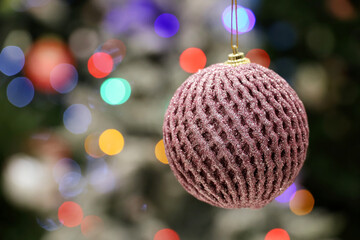 Christmas toy ball hanging on background of blurred festive lights. New Year decorations, winter holidays