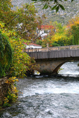 Fototapeta premium Small rustic bridge crossing the river and colorful autumn leaves. Beautiful autumnal landscape.