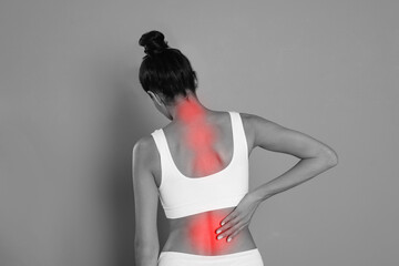 Woman suffering from back pain on grey background