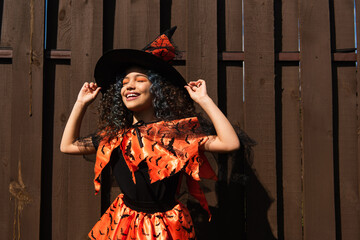 Positive kid holding witch hat during halloween celebration outdoors