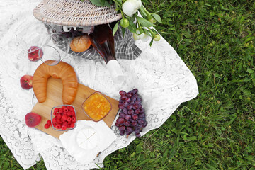 Picnic blanket with tasty food, flowers and cider on grass outdoors, flat lay