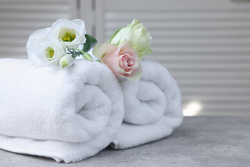 Fototapeta na wymiar Rolled towels and flowers on grey table indoors
