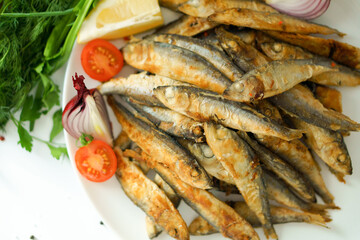 Fried small herring is laid out on a white plate.