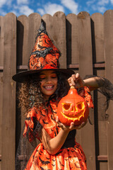 happy curly girl in halloween costume and witch hat holding carved pumpkin