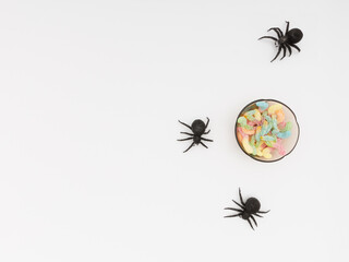 Some black toy spiders and a bowl full of candy. White background