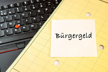 Laptop keyboard and yellow Folder map with sticky note message, paper note Buergergeld. Citizens' allowance instead of Hartz IV concept. changes for the unemployed in germany