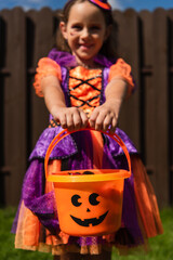 selective focus of trick or treat bucket in hands of girl in clown costume smiling on blurred background