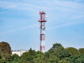 Samotnie wystająca wieża GSM sponad zielonych drzew na tle błękitnego nieba i prawie bezchmurnej pogody
