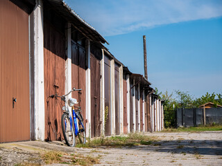 Samotnie stojący rower przy starych garażach osiedlowych na tle błękitnego niemalże...