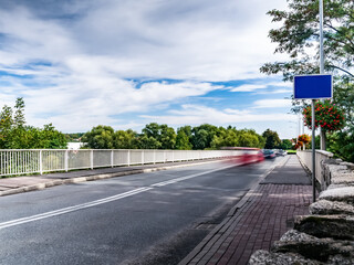 Długa ekspozycja drogi prowadzącej przez most nad odrą, poruszające się rozmyte samochody, w tle błękitne niebo spowite pochmurną pogodą