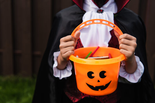 cropped view of boy in halloween costume holding trick or treat bucket with sweets
