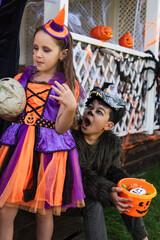 boy in werewolf costume holding bucket with candies and grimacing near girl with skull