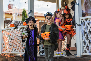 Positive multiethnic children holding skull and bucket during halloween celebration with friends...