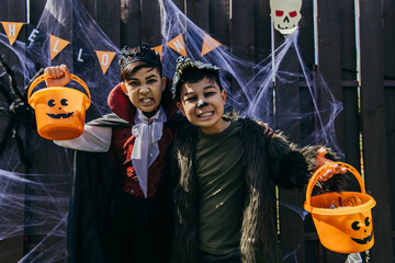 Asian kids with makeup grimacing at camera while holding buckets during halloween party outdoors