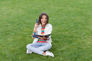 surprised teen girl making notes in notebook sitting on grass. taking notes. student make notes