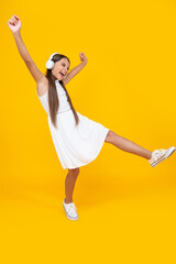 Fototapeta na wymiar teen child listen music in headphones and dancing on yellow background