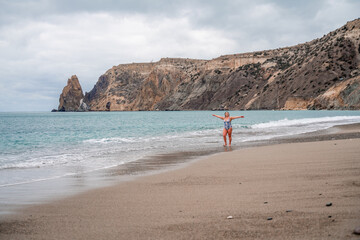 A plump woman in a bathing suit enters the water during the surf. Alone on the beach, Gray sky in the clouds, swimming in winter.
