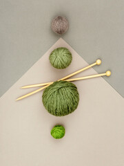 Row of woollen green and grey coloured balls of soft natural yarn placed near wooden knitting needles on graphic grey background. Craft, DIY and handmade concept. Winter hobby background.