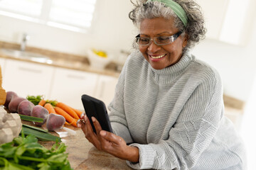 Senior african american women cooking alone in the kitchen and using smartphone