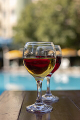 Two glasses of wine on a wooden table next to the swimming pool in summer. Relaxing vacation,    holiday and happy weekend concept.