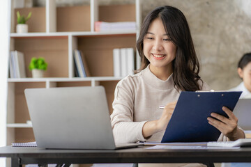 A new generation of Asian female accountants are calculating. Attractive office worker saving, finance and economic concepts to write notepads placed on desktop.