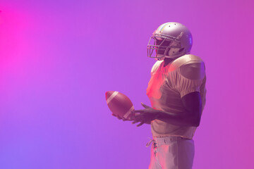 African american male american football player holding ball with neon pink and purple lighting