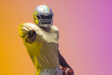 African american male american football player holding ball with neon yellow and purple lighting