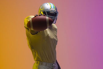African american male american football player holding ball with neon yellow and purple lighting