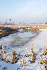 Frozen pond in the meadow. Winter time with snow on fields.