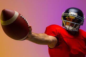 Caucasian male american football player holding ball with neon yellow and purple lighting