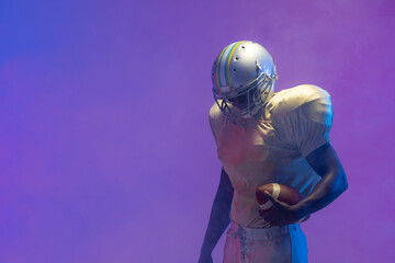 African american male american football player holding ball with neon blue lighting