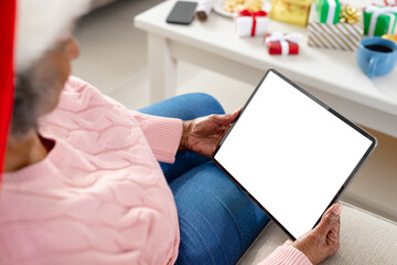 Happy senior african american women wearing santa claus hat and holding tablet with copy space