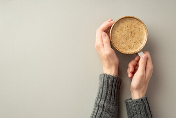 Autumn mood concept. First person top view photo of woman's hands in knitted sweater holding cup of fresh frothy drinking on isolated grey background with empty space - Powered by Adobe