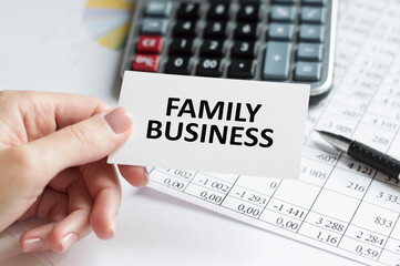 FAMILY BUSINESS text on a card on the background of an office desk in the hand of a user, a business concept