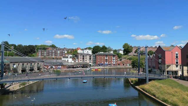 Exeter Quay on a summers day, flying over the River Exe Bridge while people walk by and a flock of birds pass the camera. Drone Video. 30fps.