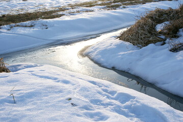Winter view of field - meadow. Grass covered by snow. Frozen drainage ditch.