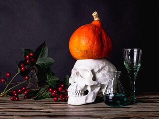 Gloomily Halloween still life with skull, pumpkin, rowan and test tubes with green liquid.