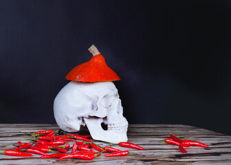 Halloween melancholyc still life with skull, pumpkin and red pepper on a black background witj copy space.