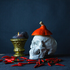 Halloween dark still life with skull, candle, pumpkin and red pepper on a dark blue background witjh copy space.