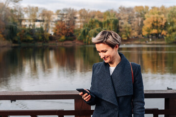 Fototapeta premium A woman in a city park by the river uses a smartphone