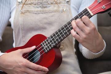 Young woman playing red ukulele at home, sitting on the floor, dressed as a hipster, learning songs