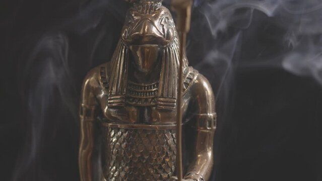 golden statue of the Egyptian god Ra in smoke on a black background