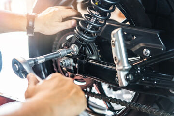 Mechanic using a wrench and socket to Remove and Replace Adjustable Rear Motorcycle Suspension, working in garage maintenance, repair motorcycle concept .selective - obrazy, fototapety, plakaty