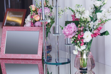 pink empty frame and flowers in a vase on a mirror table.