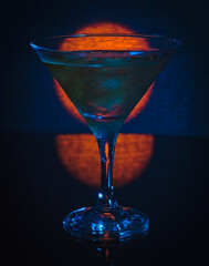 Concept photo: cocktail glass with a drink with ice, on the background of a red circle.