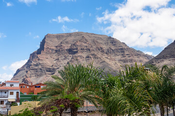 Scenic view on the massive sharp cliffs Cueva de Cabras and mountains in Valle Gran Rey, La Gomera, Canary Islands, Spain, Europe. Palm trees are in the foreground. Clear sky on a sunny summer day